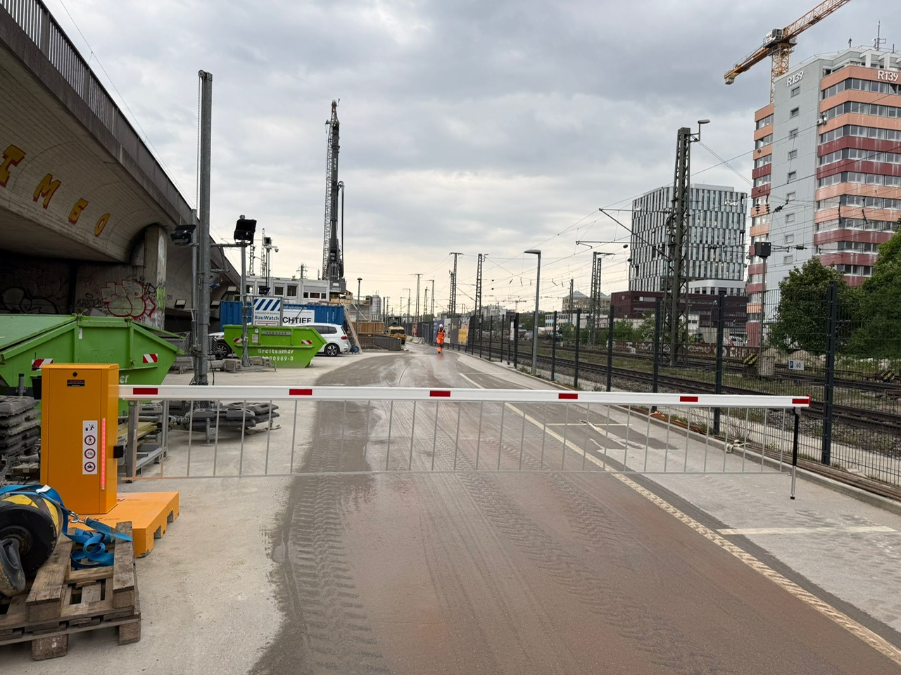 Mobile Schranke vor einer Baustelle, im Hintergrund Bahngleise und Industrie