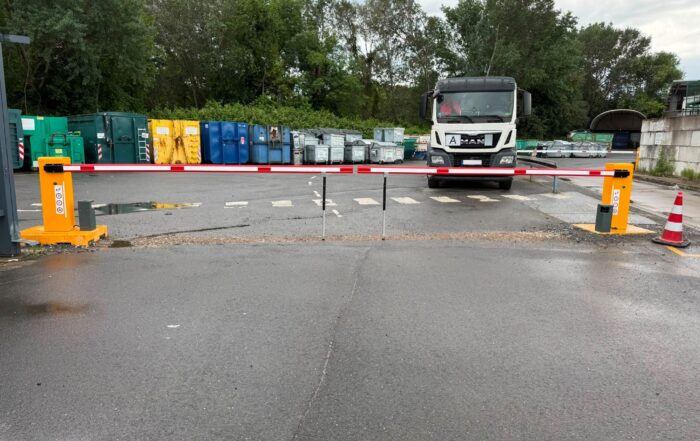 automatische Schranken, dahinter ein LKW und verschiede Müllcontainer