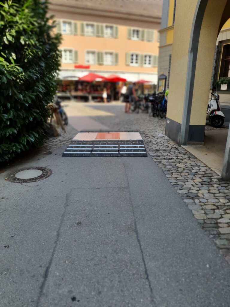 Fahrzeugsperre ARMIS ONE liegt auf einem Weg, dahinter ein Marktplatz