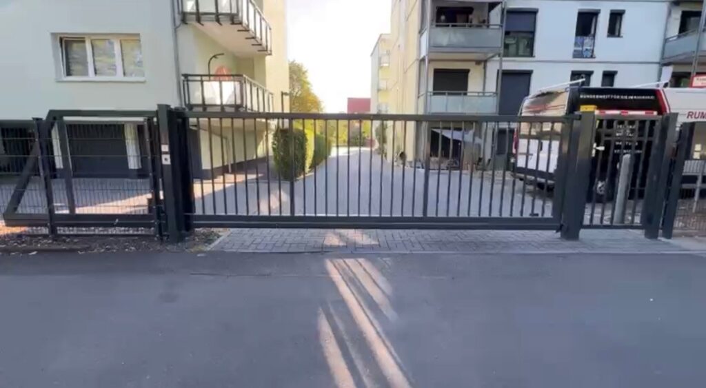 Dunkelgraues Schiebetor vor einer Wohnanlage, dahinter ein Handwerkerauto