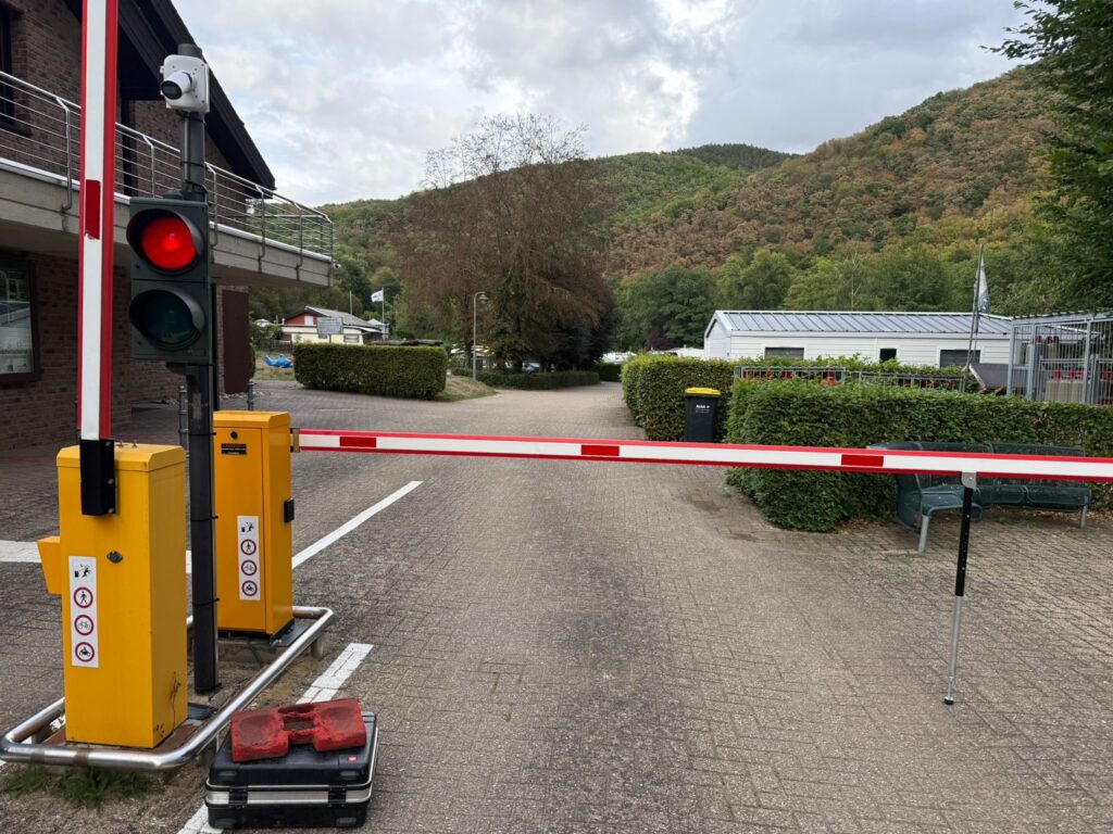 Zwei Schranken, die eine geöffnet, die andere geschlossen, vor einer Zufahrt, daneben eine dazugehörige Ampel