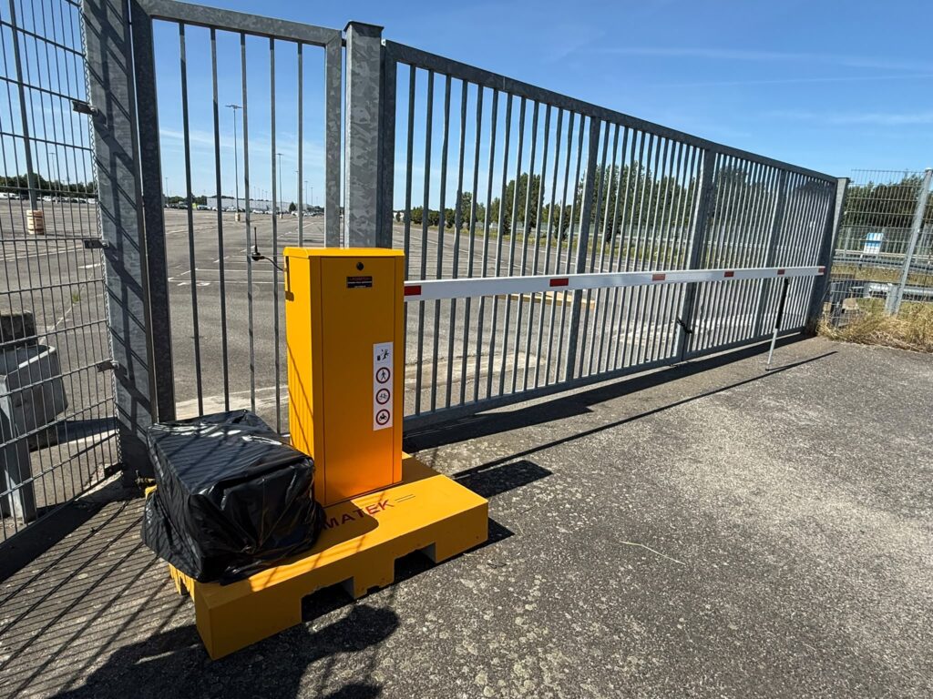 eine orangene Schranke vor einem geschlossenen Metalltor