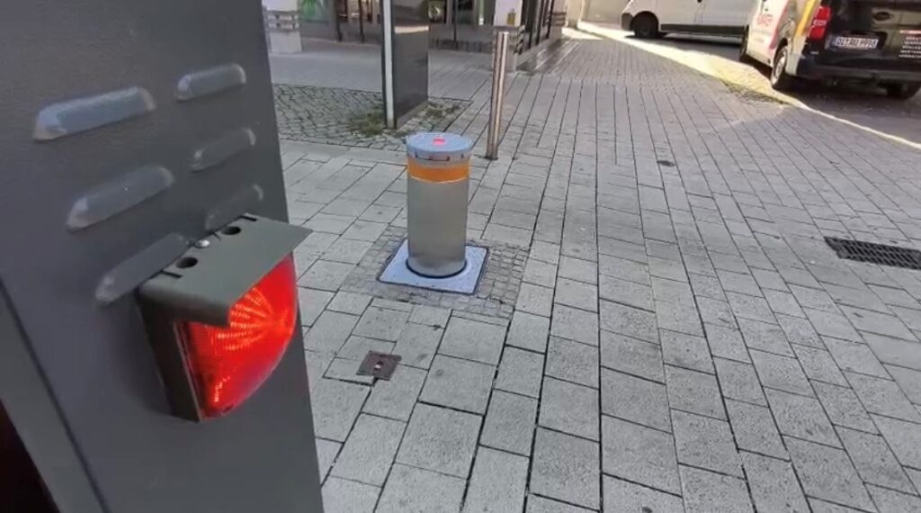 Ein versenkbarer Edelstahlpoller, davor eine Säule mit roter Ampelleuchte