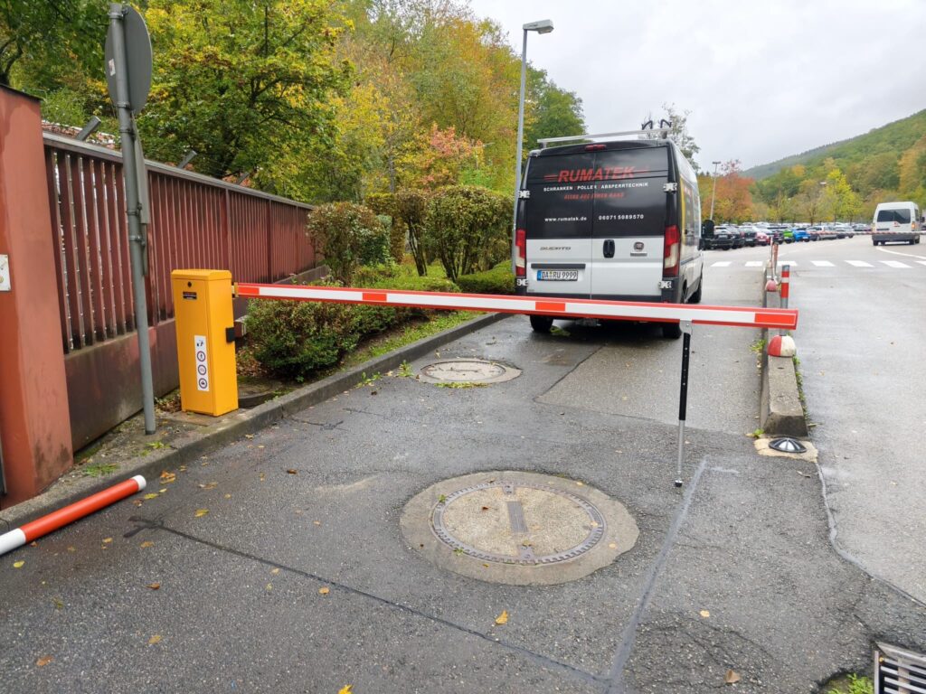 Eine geschlossene orangene Schranke, dahinter ein beschrifteter Kleintransporter