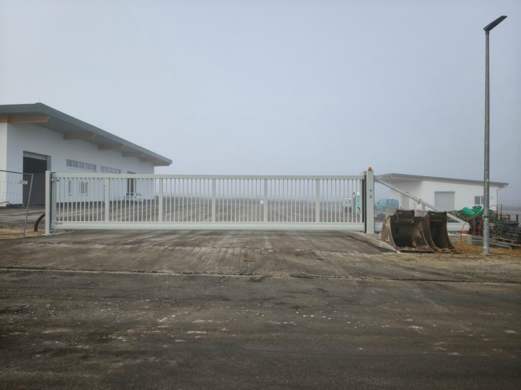 weißes Schiebetor vor einem Betriebsgelände, dahinter Nebel