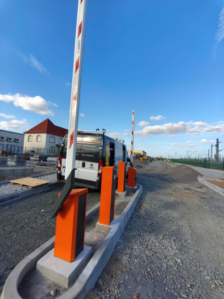 Magnetic Schranken und Bediensäulen in orange vor einer Schottereinfahrt zu einem Parkplatz